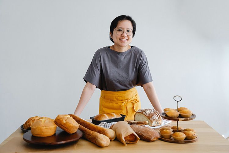 a woman smiling stood in front of table with a range of bread products on top