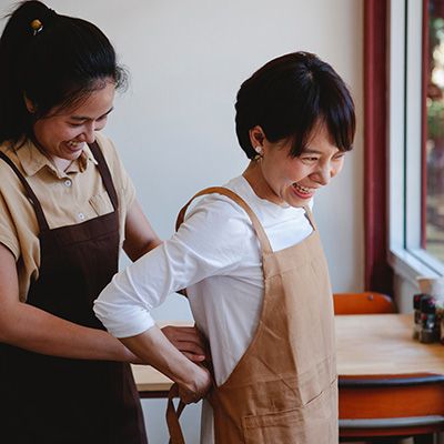 two women smiling as one puts an apron on the other